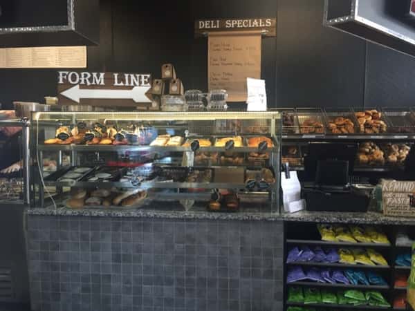 Front counter of store showing a glass with pastries behind it & a sign that says "Form line"