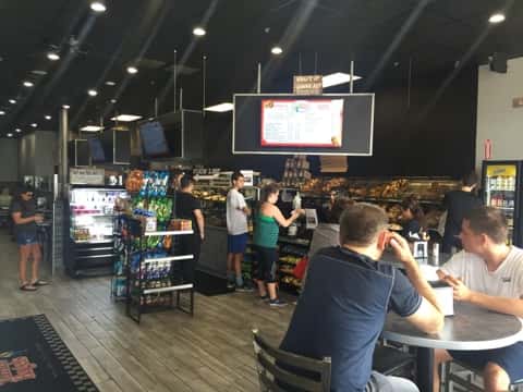 Inside of store with customers sitting at a table and other customers checking out at the cash register