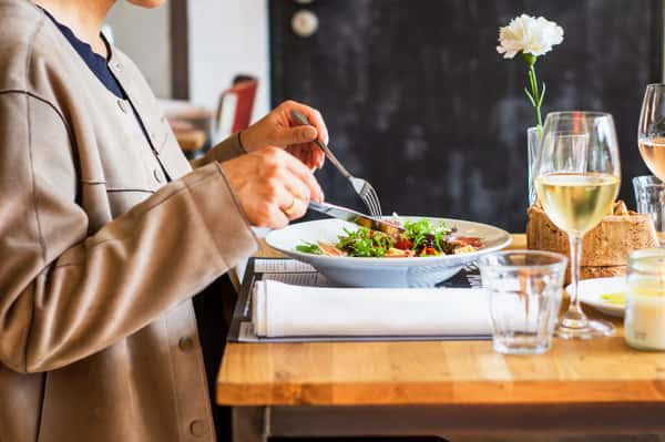 A woman sitting at a table using a fork and knife to eat a meal