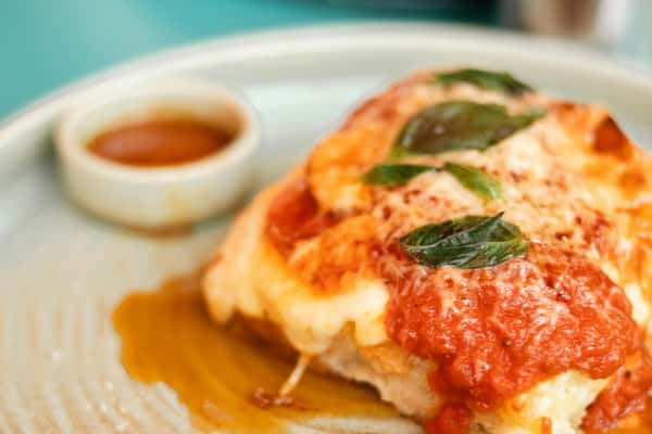 Cheesy lasagna topped with tomato sauce and basil leaves served on a plate with a small dish of sauce.