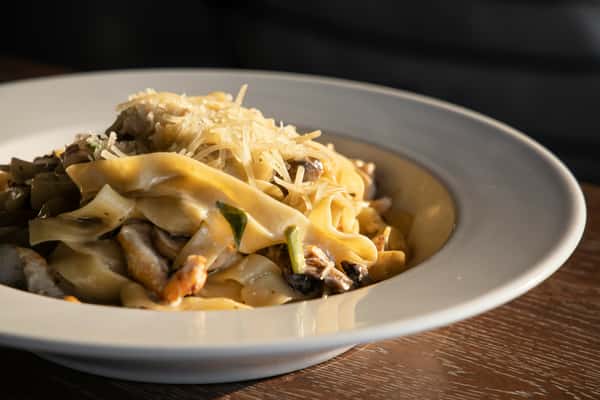 Fettuccine pasta with mushrooms, zucchini, and grated parmesan in a creamy sauce served in a white bowl.