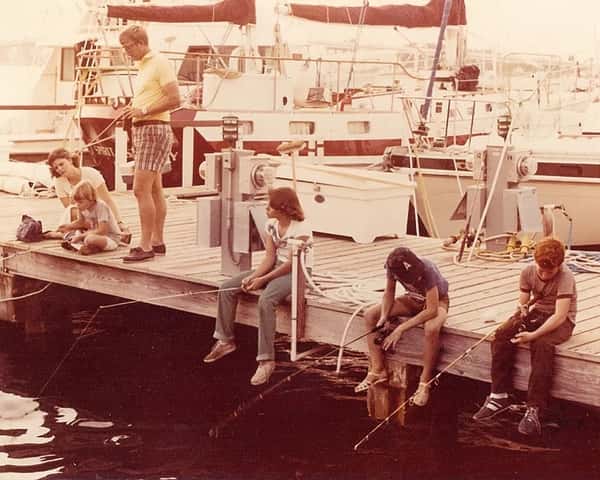 A fishing dock with individuals sitting on the edge, engaging in fishing activities near several boats.