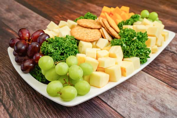 Cheese and cracker platter with cubed cheddar and jack cheese, green and red grapes, and leafy greens for garnish.