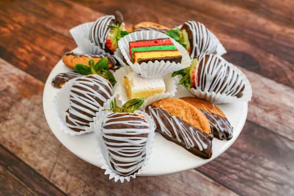 Dessert platter with chocolate-dipped strawberries, rainbow cookies, biscotti, and chocolate fudge brownies on a white stand.