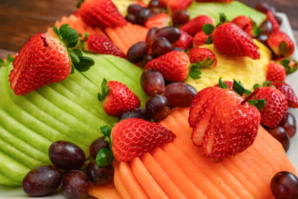 Sliced cantaloupe, honeydew, and pineapple topped with fresh strawberries and grapes on a fruit platter.