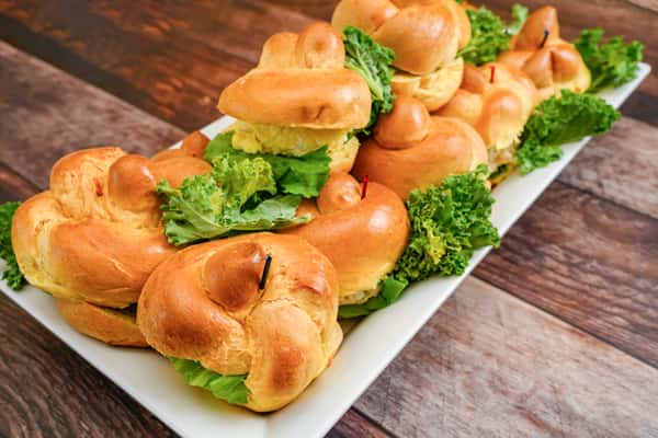 Mini sandwiches with lettuce and filling on golden knot rolls, neatly arranged on a white rectangular platter.