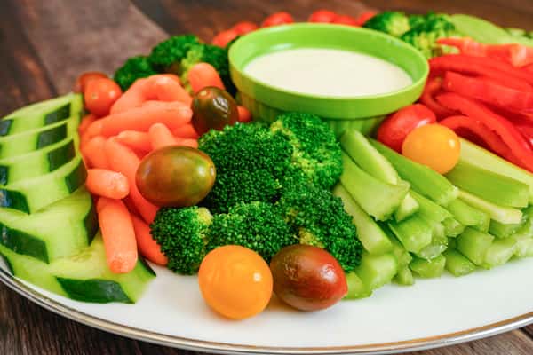 Colorful veggie platter with broccoli, celery, cherry tomatoes, cucumber, carrots, red bell pepper, and a ranch dip in the center.