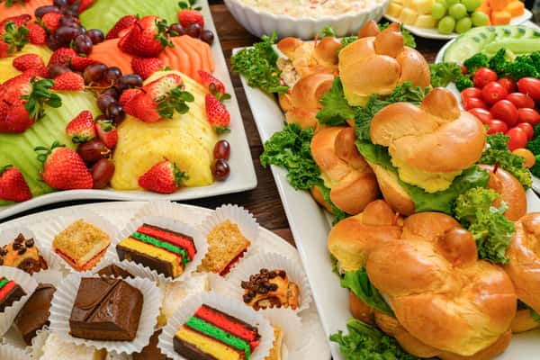 Assorted party spread with chicken salad sandwiches, fresh fruit, veggie platter with dip, and colorful bite-sized desserts.