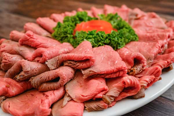 Platter of thinly sliced roast beef arranged in a circle, garnished with leafy greens and a tomato rose centerpiece.
