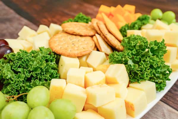 Assorted cheese cubes with crackers, green grapes, and leafy garnish arranged on a rectangular platter.