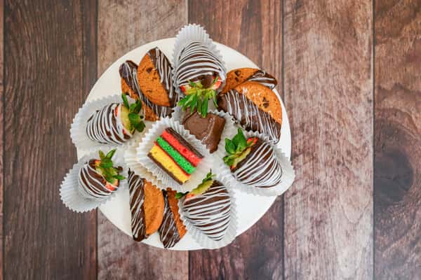 Dessert platter with chocolate-dipped strawberries, rainbow cookies, biscotti, and chocolate fudge brownies on a white stand.