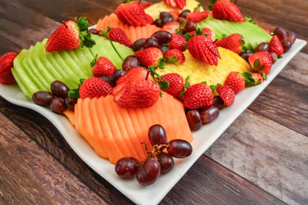 Sliced honeydew, cantaloupe, and pineapple topped with fresh strawberries and red grapes on a white serving platter.