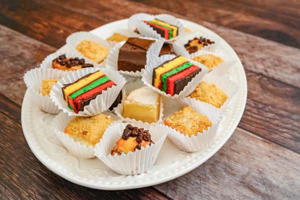 Dessert platter with chocolate-dipped strawberries, rainbow cookies, biscotti, and chocolate fudge brownies on a white stand.