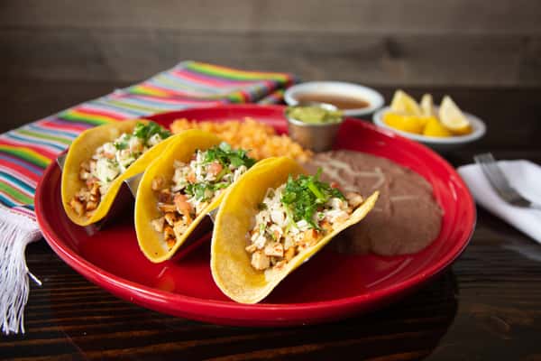 Gemini said Three street tacos in yellow corn tortillas, topped with onions and cilantro, served with rice, beans, and guacamole on a red plate.