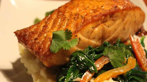 Pan-seared salmon fillet served over mashed potatoes with sautéed spinach, bell peppers, and fresh cilantro garnish.