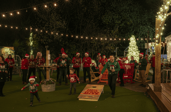 Families in Christmas sweaters and Santa hats play cornhole under string lights by a glowing tree at an outdoor holiday gathering.