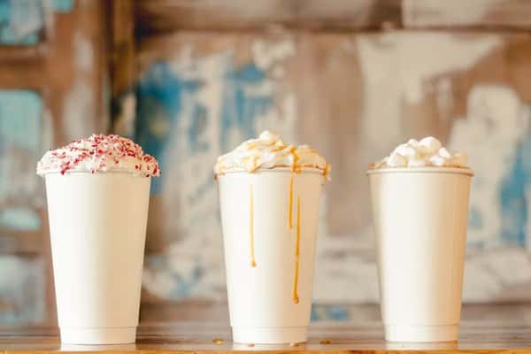 Three whipped cream-topped drinks in white cups with crushed peppermint, caramel drizzle, and marshmallows.
