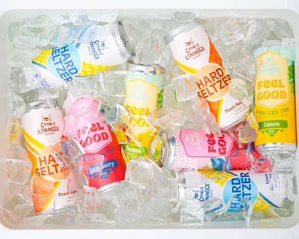 Colorful Crooked Hammock hard seltzer and Feel Good tea cans packed in ice inside a white cooler.