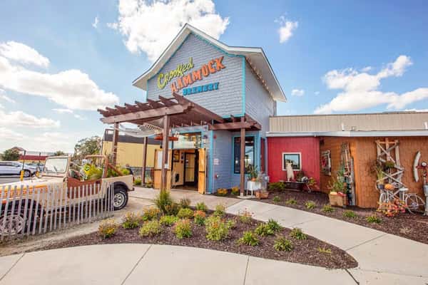 Exterior of Crooked Hammock Brewery with a colorful entrance, decorative garden, and a vintage Jeep parked nearby.