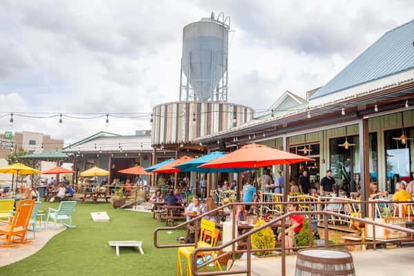 Crowded patio at Crooked Hammock Brewery with colorful umbrellas, cornhole game, and diners enjoying food and drinks.