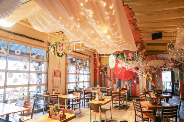 Indoor dining area with wooden tables, festive holiday decor, hanging snowflakes, string lights, and draped white fabric on ceiling.