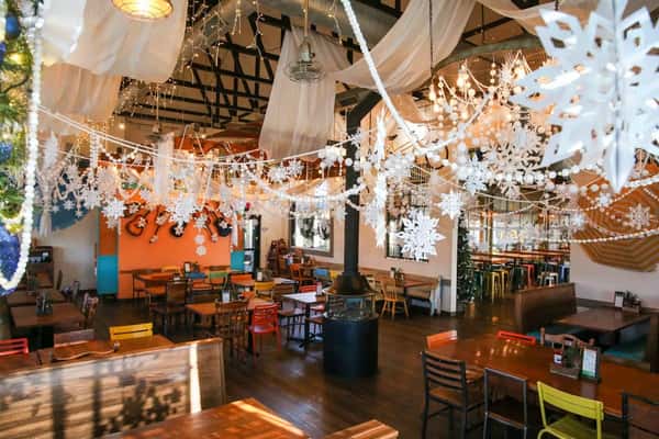 Dining area with hanging snowflakes, string lights, and sheer drapery in a cozy, festive winter-themed restaurant setting.