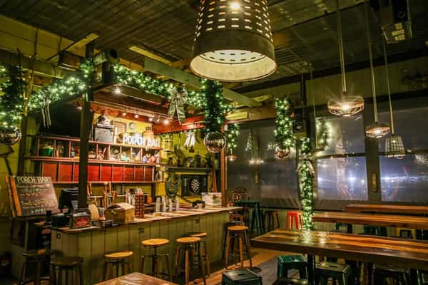 Porch Bar with garlands, wood stools, hanging lights, and cozy rustic decor during the holiday season.