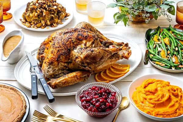 Golden roasted turkey surrounded by mashed sweet potatoes, green beans, cranberry sauce, and pie on a festive holiday table.