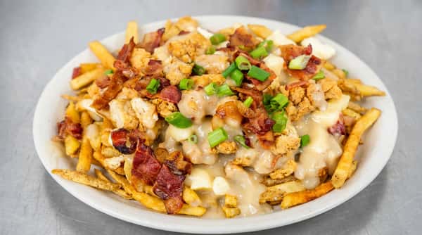 Poutine with golden fries, brown gravy, white cheese curds, crispy bacon, fried chicken pieces, and green onions.