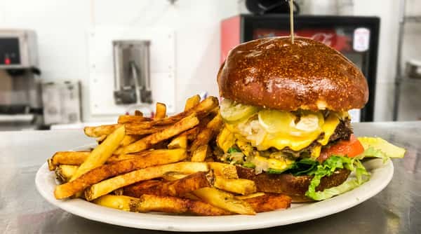 A cheeseburger with two patties, melted cheese, pickles, onions, lettuce, and tomato, served with a side of french fries.