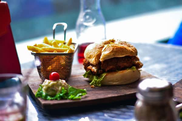 Burger with lettuce served on a wooden board, accompanied by French fries in a metal basket and a small side salad on a restaurant table.