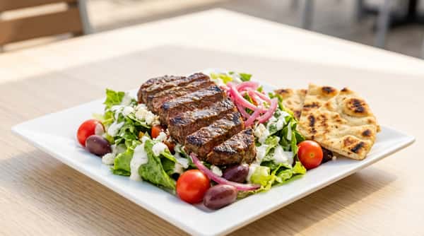Steak salad with mixed greens, olives, feta, cherry tomatoes, pickled onions, and white dressing, served with pita bread.