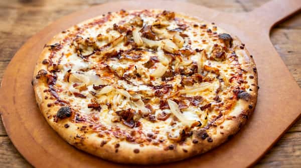 Round pizza with melted cheese, caramelized onions, and chopped meat on a wooden peel.