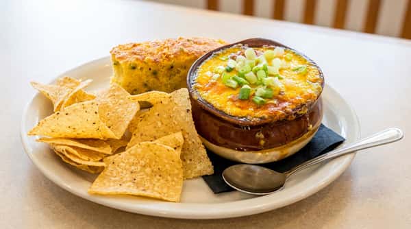 Bowl of chili topped with cheese and green onions, served with tortilla chips and cornbread.