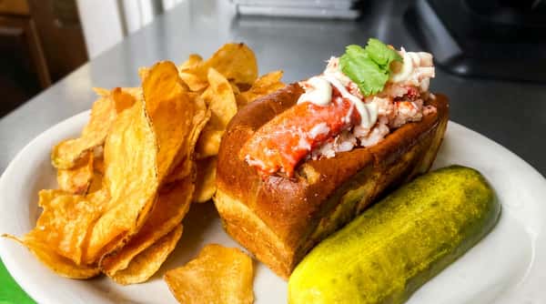 Lobster roll with mayo and cilantro, served with potato chips and a pickle.