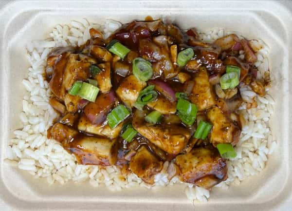 Glazed chicken bites with green onion garnish over rice in a takeout container