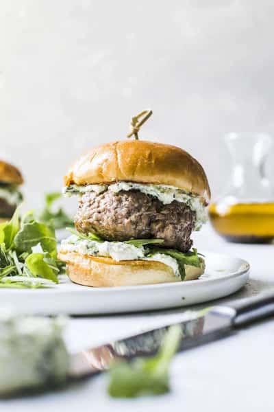 Gourmet beef burger with herbed cheese spread and fresh arugula on a toasted brioche bun, served on a white plate