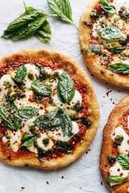 Margherita flatbread pizzas with melted mozzarella, fresh basil, and tomato sauce on a light stone surface