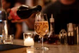 Sparkling wine being poured into a glass at a dimly lit bar with warm ambiance