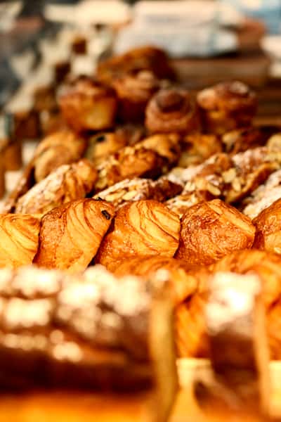Assorted golden pastries and croissants displayed in a bakery with warm lighting