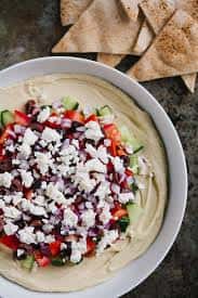 Creamy hummus topped with diced vegetables and crumbled cheese, served with pita chips