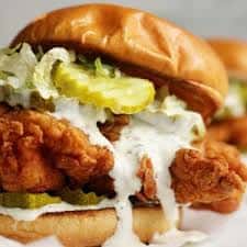 Close-up fried chicken sandwich with creamy sauce and pickles on a toasted bun
