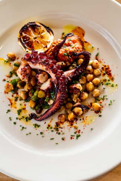 Grilled octopus with chickpeas, charred lemon, and herbs plated in a modern seafood dish