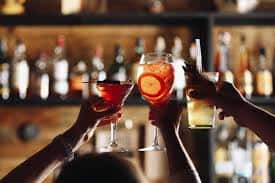 Friends toasting colorful cocktails at a bar, featuring martinis and citrus drinks in a lively nightlife setting