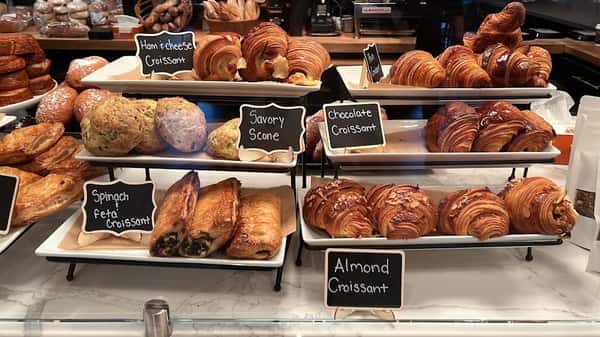 Bakery display case with croissants, scones, and pastries labeled for selection