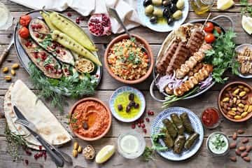 Mediterranean mezze spread with grilled skewers, dips, stuffed grape leaves, flatbread, and assorted small plates on a rustic table