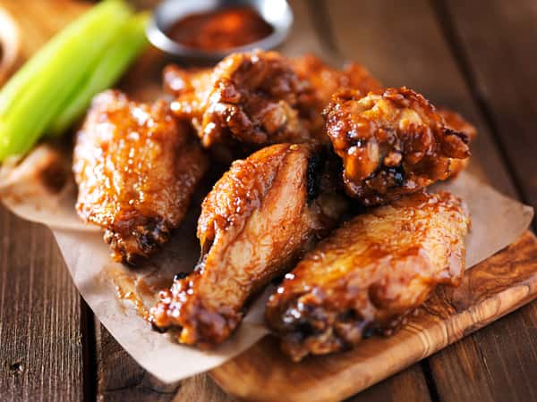 Glazed chicken wings on parchment with celery sticks and dipping sauce in the background.