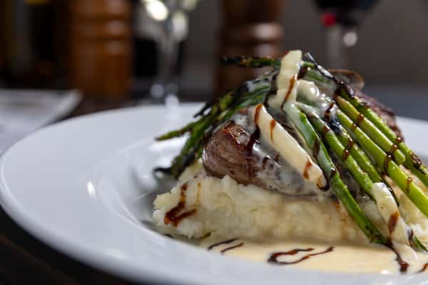 Grilled steak over mashed potatoes topped with asparagus, drizzled with creamy white sauce and balsamic glaze.