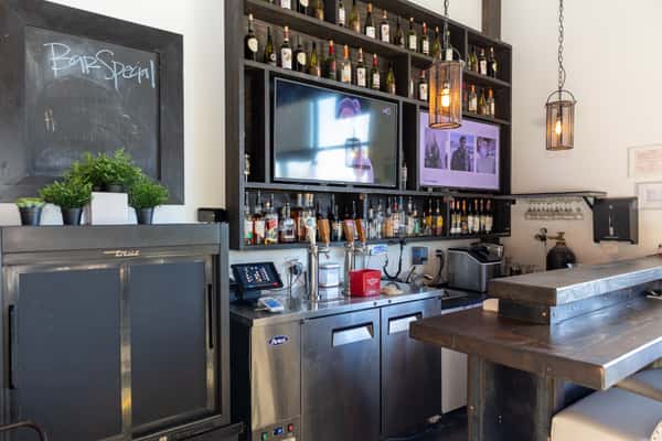 Contemporary bar area with flat-screen TVs, a variety of liquor bottles, hanging pendant lights, and a rustic wood countertop.