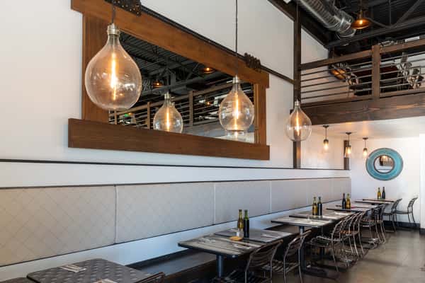 Modern Italian bistro interior with industrial lighting, wood and metal accents, cozy booth seating, and a mezzanine dining area.